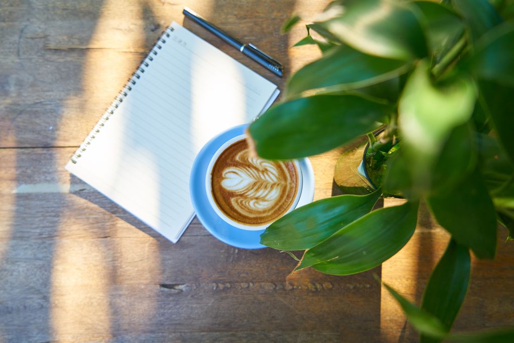 Flat lay of a latte and notebook on a wooden table with natural light.